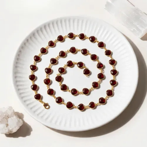 Faceted garnet gemstone chain necklace on a white dish — January birthstone jewelry