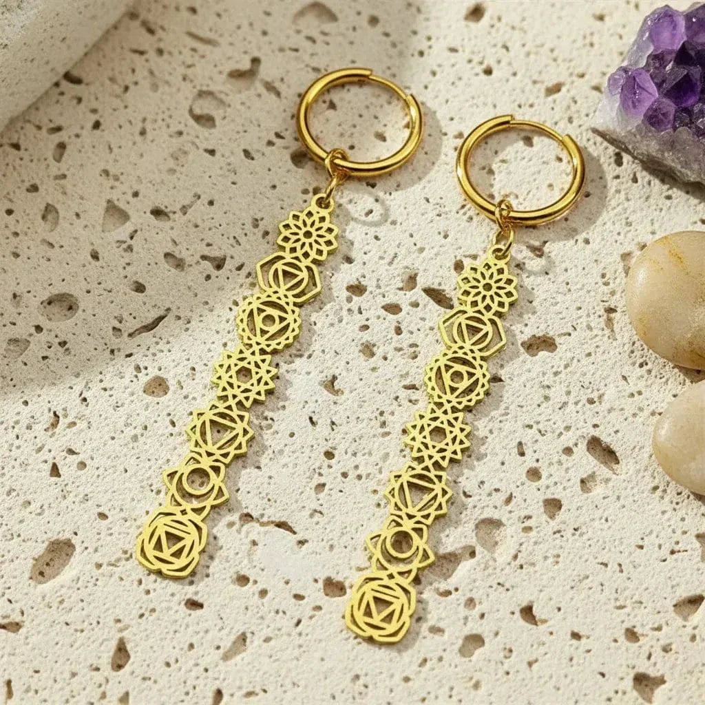 gold 7 chakra symbols earrings on light colored stone