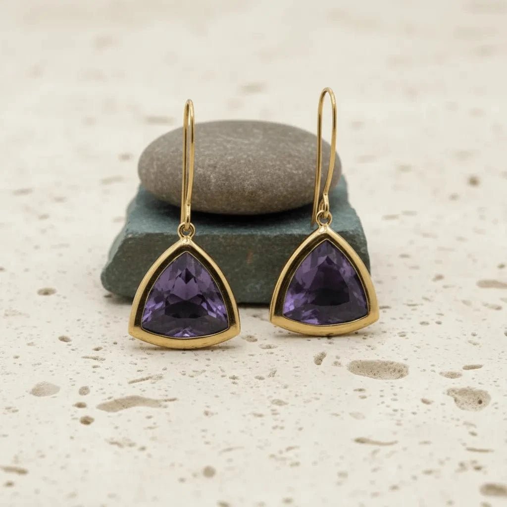 Gold-trimmed purple gemstone earrings on a textured surface with stones.