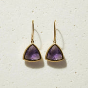 Gold earrings with purple gemstones on a textured white background