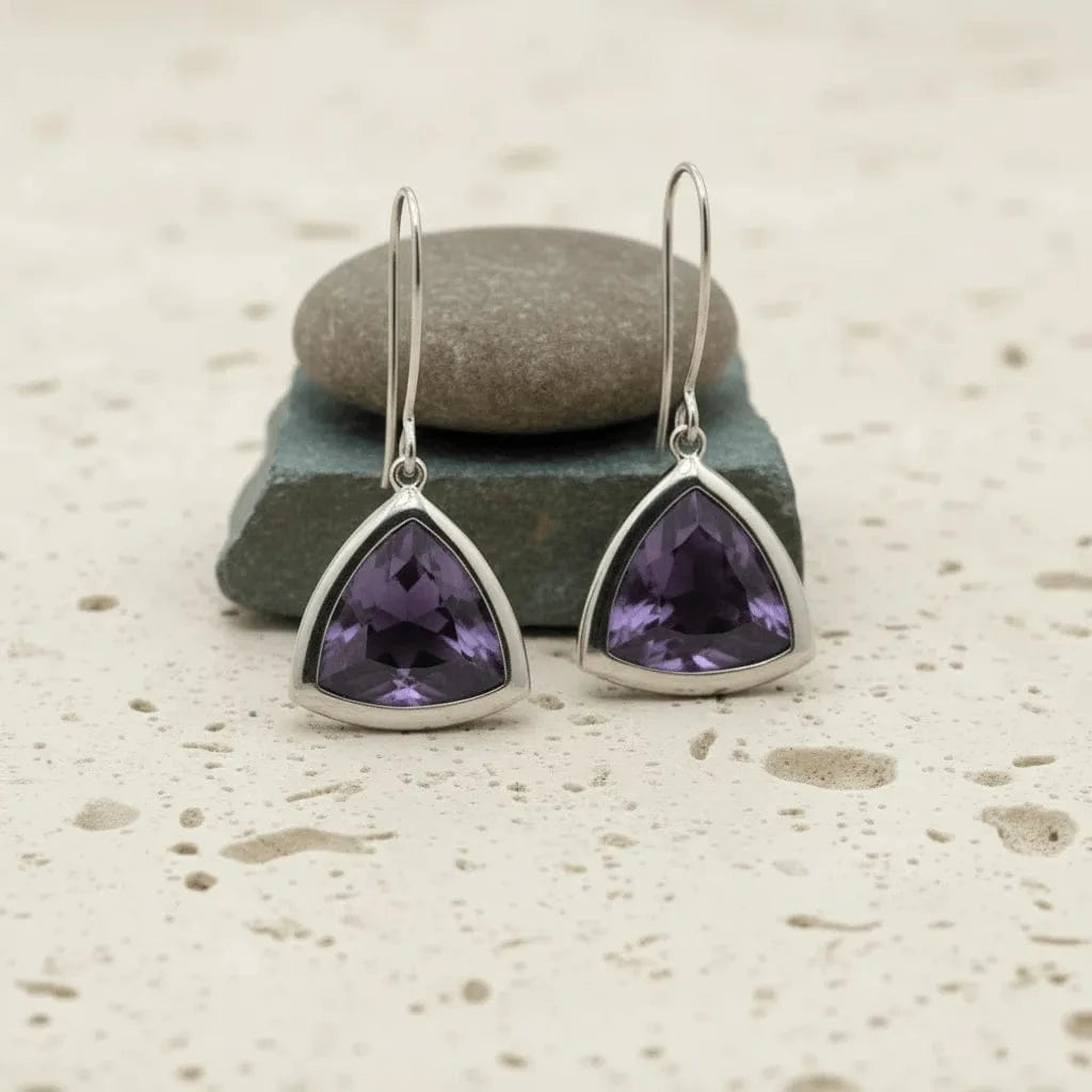 Pair of silver earrings with purple gemstones on a stone surface