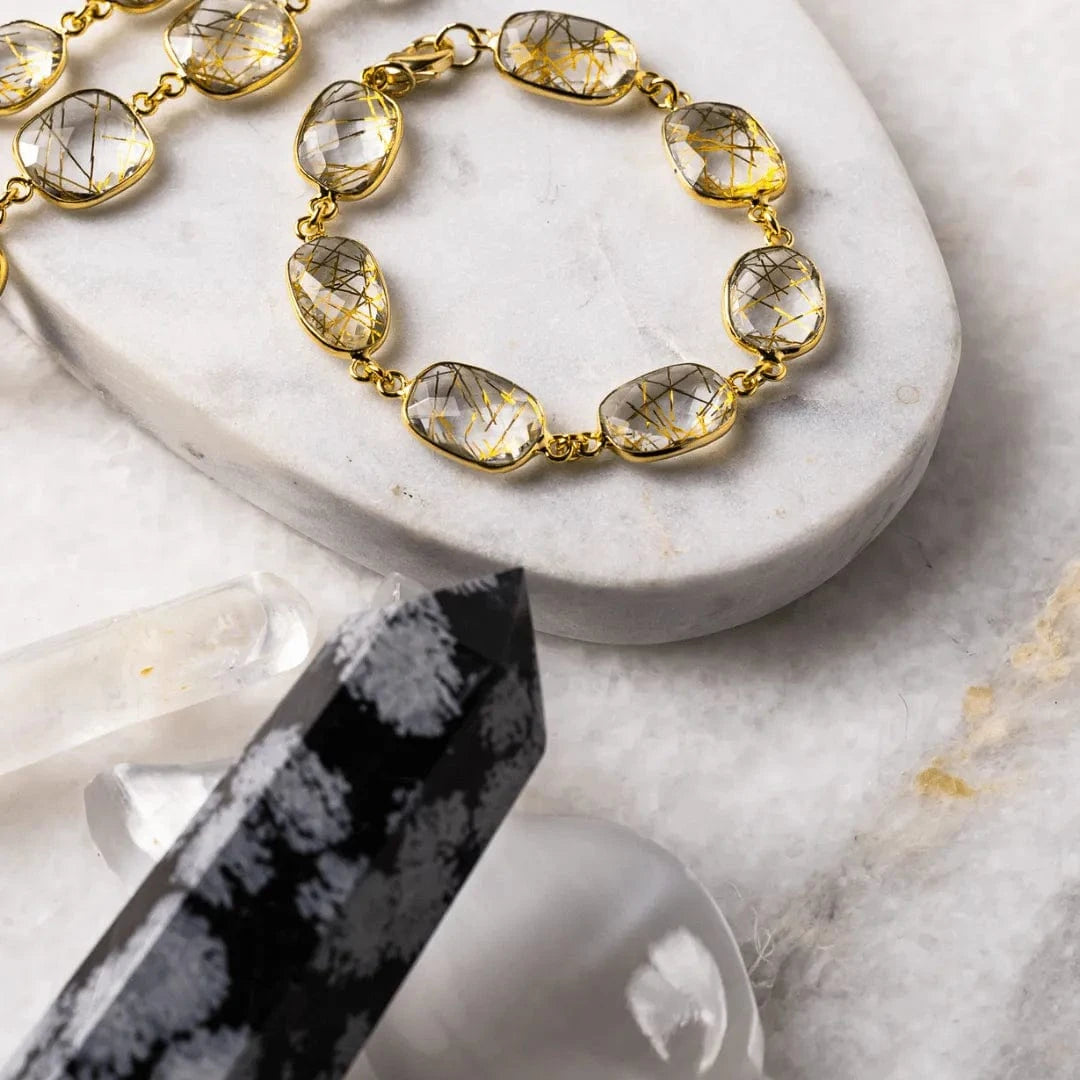 Gold bracelet with clear gemstones on a marble surface