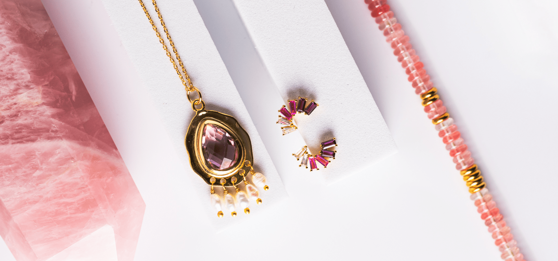 flat lay photo of rose quartz crystal, pink sapphire studs, rose quartz beaded bracelet and pink topaz pearl necklace