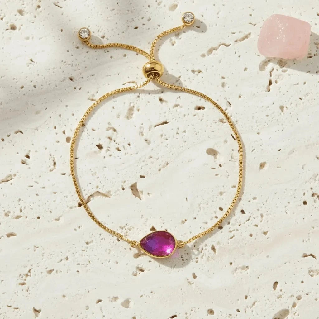 Gold bracelet with a pink gemstone on a textured beige surface