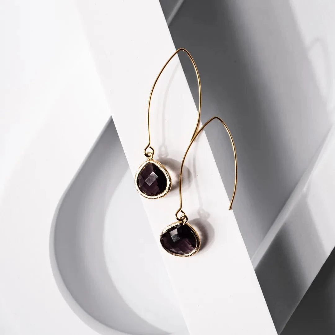 Gold earrings with dark gemstones on a white and gray geometric background