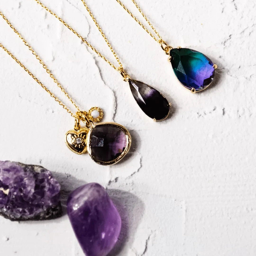 Three gold necklaces with teardrop-shaped gemstones on a textured white surface.