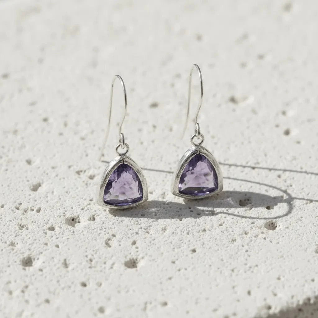 Pair of silver earrings with purple gemstones on a textured white surface