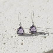 Pair of silver earrings with purple gemstones on a textured white surface