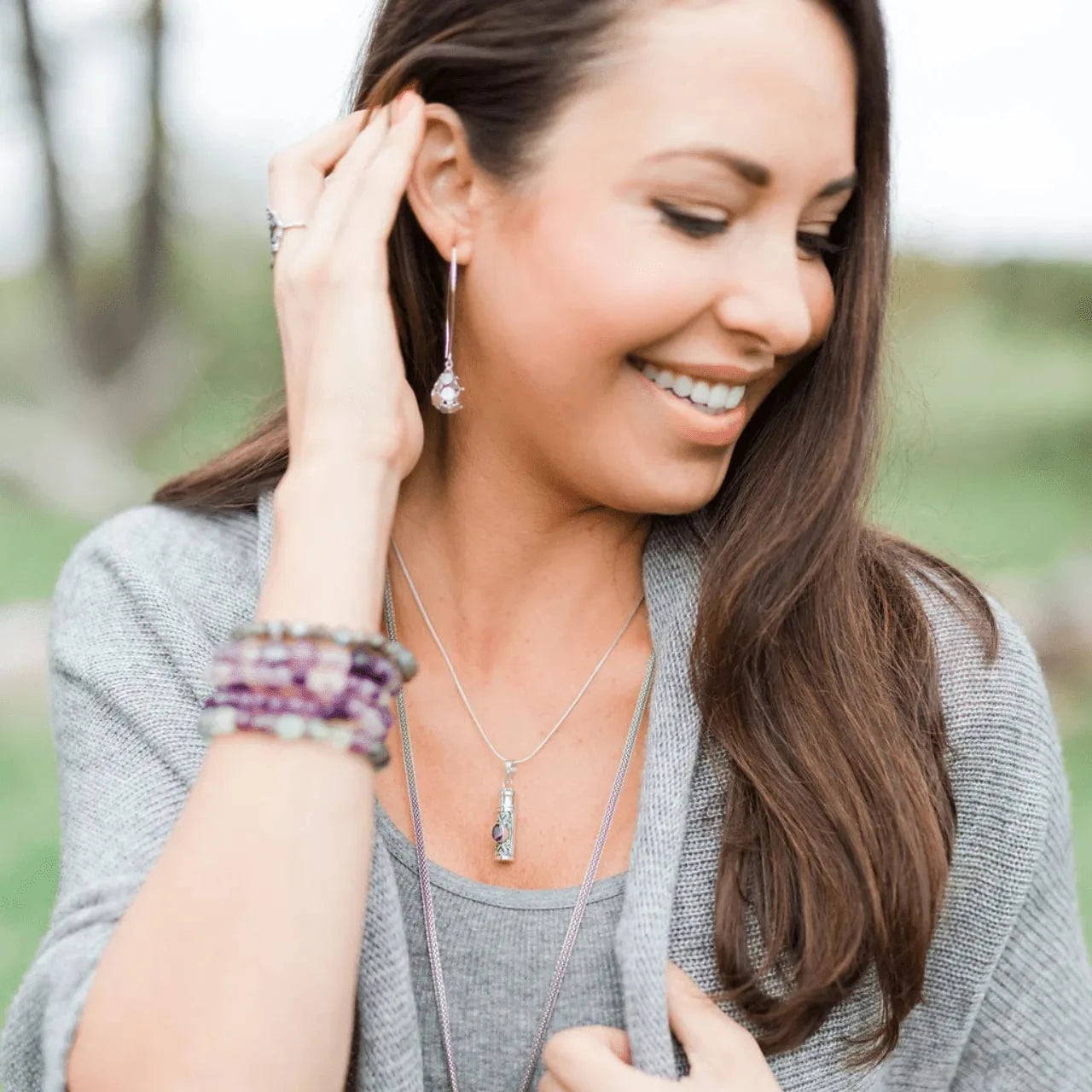 Woman adjusting an earring outdoors with a blurred natural background