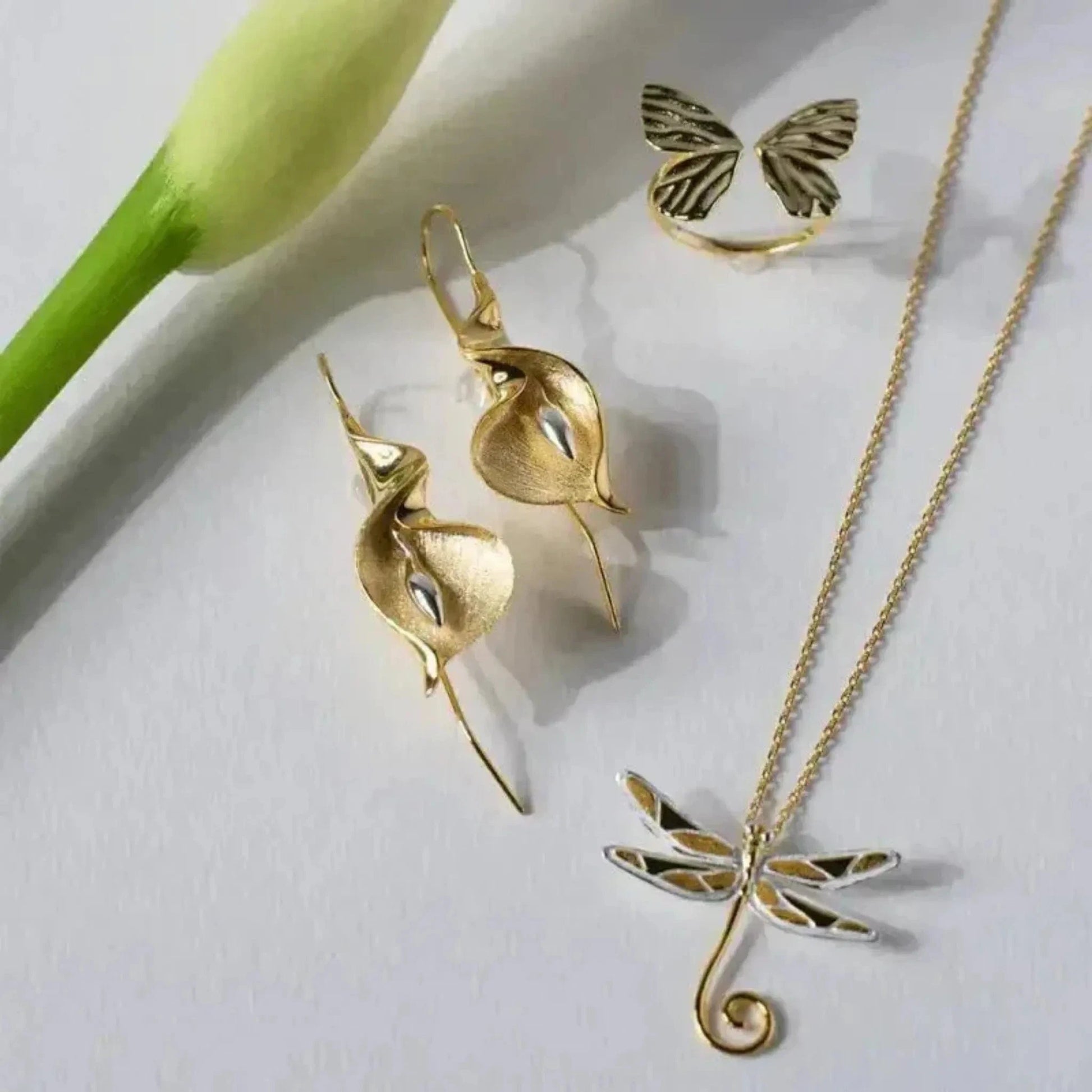 flat lay with gold cala lily earrings dragonfly necklace butterfly ring