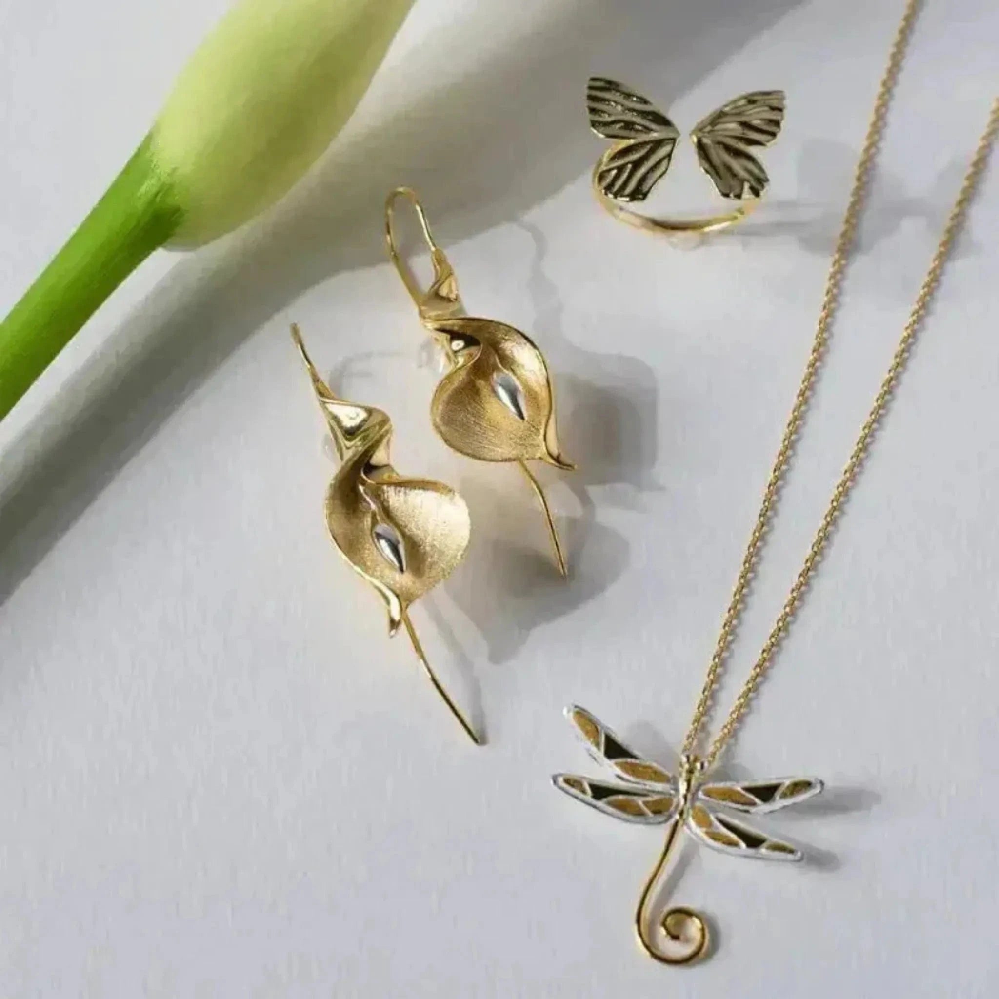 flat lay with gold cala lily earrings dragonfly necklace butterfly ring