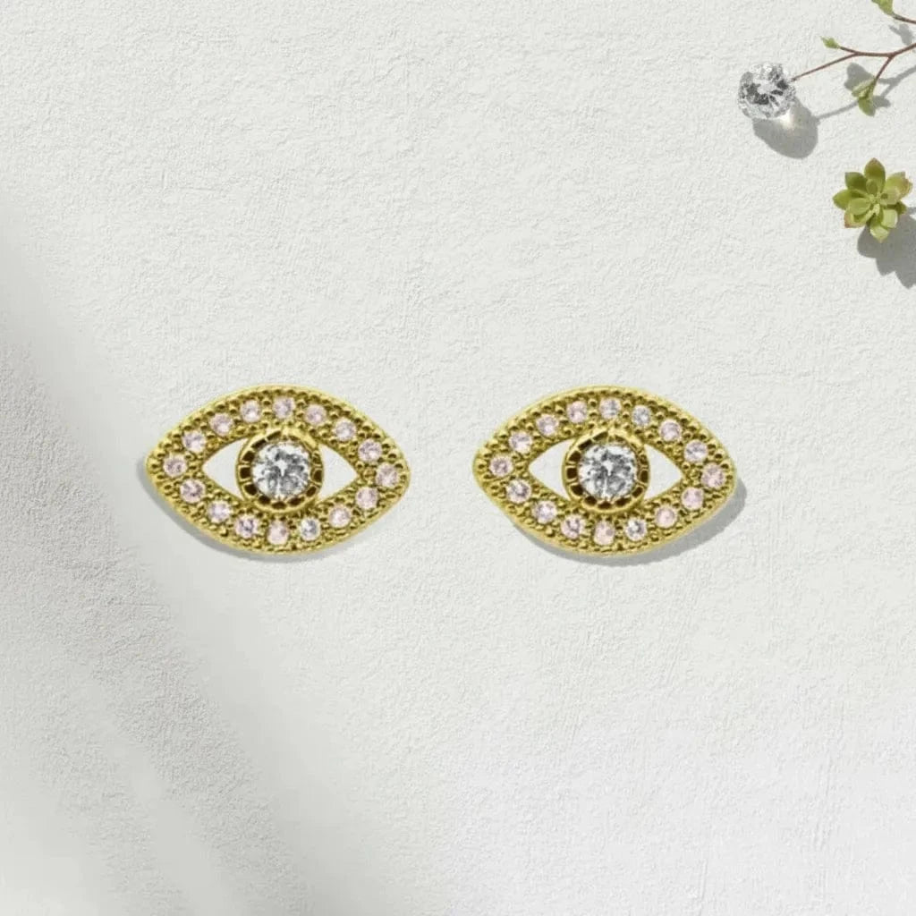 Gold eye-shaped earrings with clear gemstones on a light background