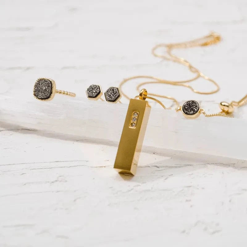 Gold jewelry set with necklace, earrings, and bar pendant on a light marble background