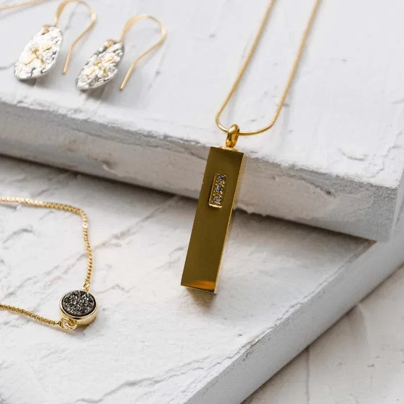 Gold necklace with a rectangular pendant on a light marble surface