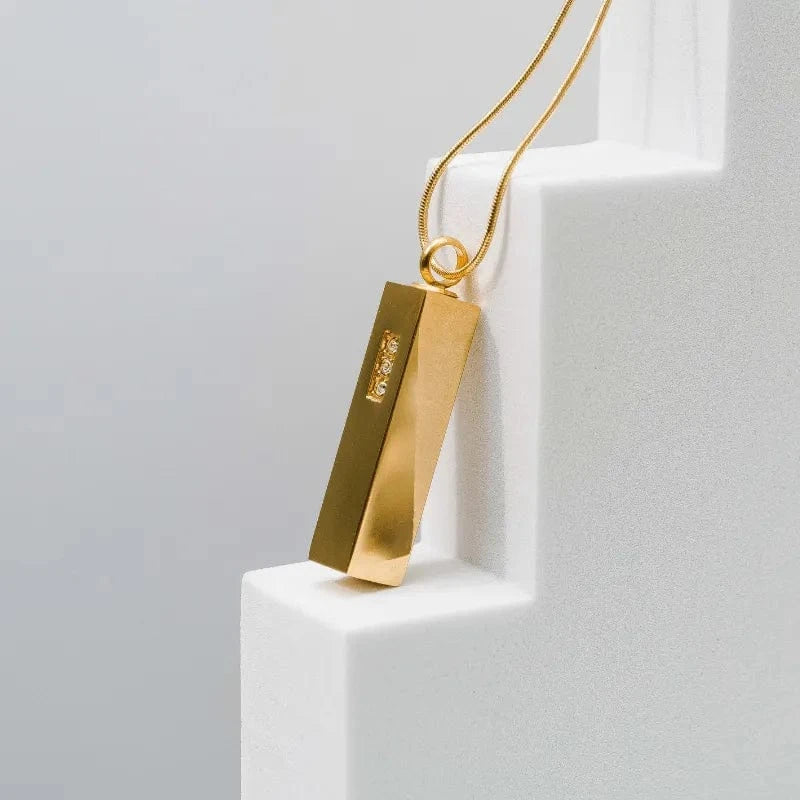Gold pendant necklace on a white pedestal with a light gray background