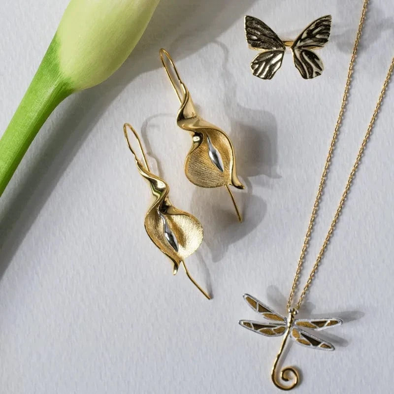 Gold butterfly and leaf-shaped jewelry on a white background with a green tulip.