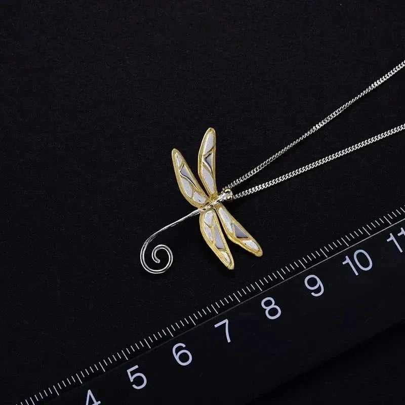 Gold and silver dragonfly pendant on a chain with a ruler for scale against a black background