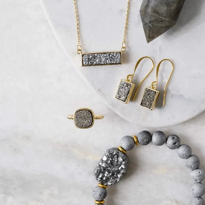 Gold and gray jewelry set including necklace, earrings, ring, and bracelet on a marble surface.