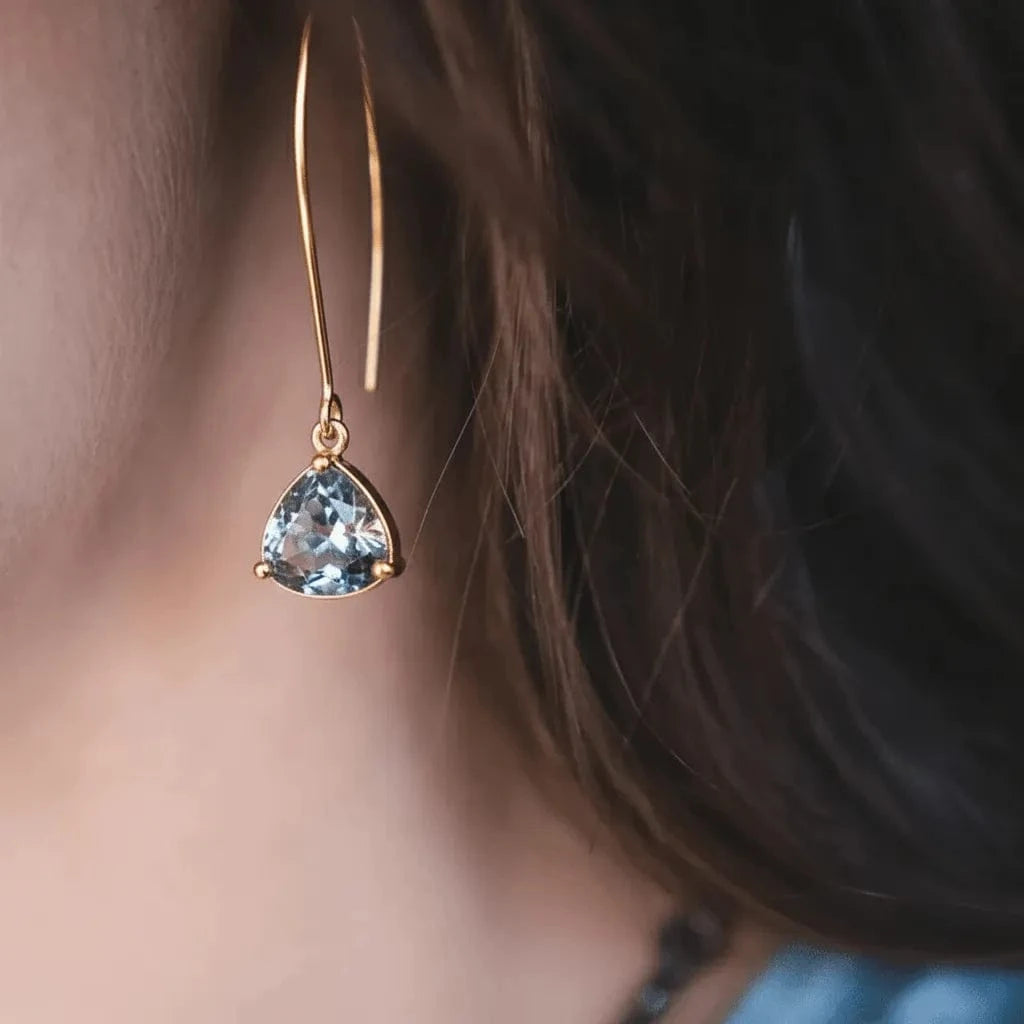 Gold earring with a blue gemstone worn by a person with dark hair.