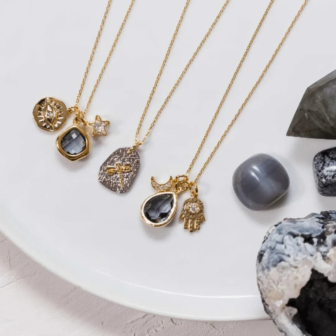 Gold necklaces with various pendants on a white surface with stones and crystals.