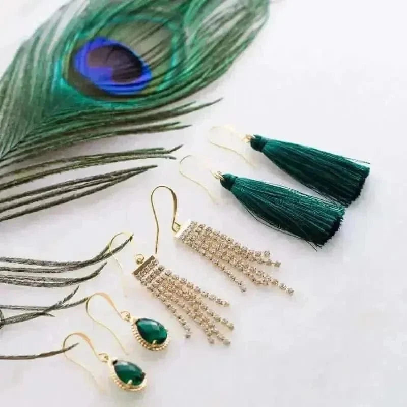 Set of earrings with green tassels and gemstones on a white surface with peacock feather.