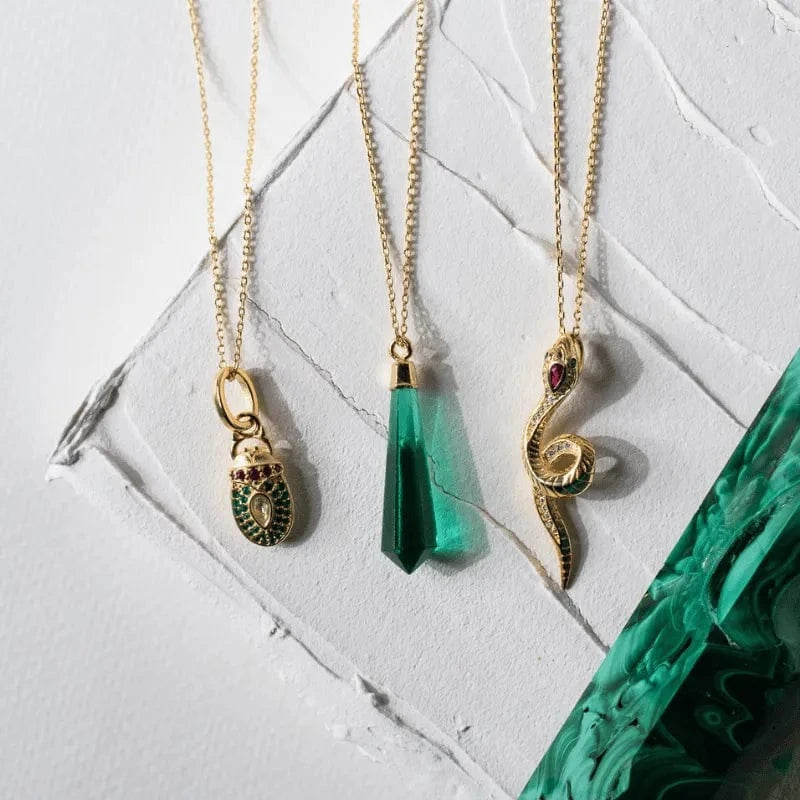 Three gold necklaces with unique pendants on a textured white surface.