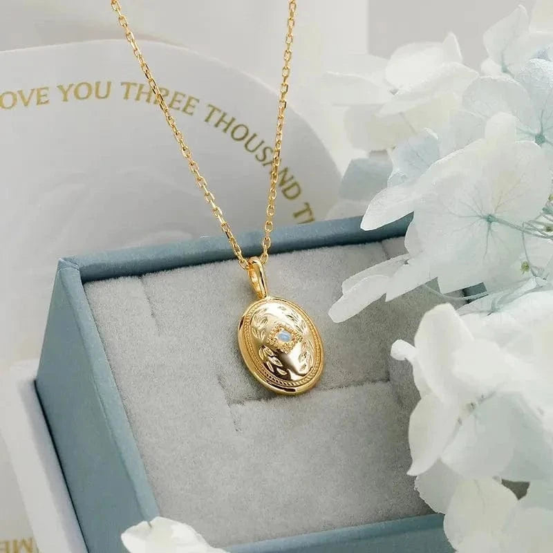 Gold necklace with a pendant in a jewelry box, surrounded by white flowers.