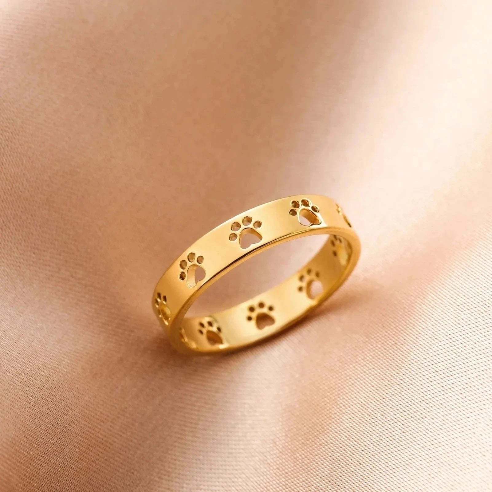 Gold ring with paw print design on a beige fabric background