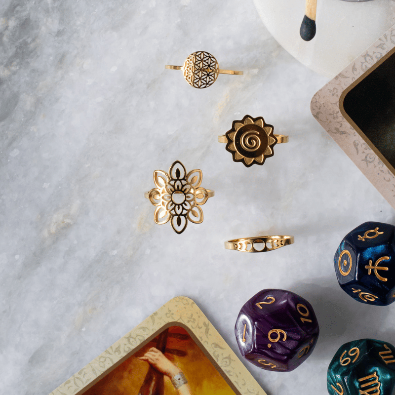 flat lay photo on white marbles, gold rings in a variety of moon and symbols, tarot cards, mystic dice