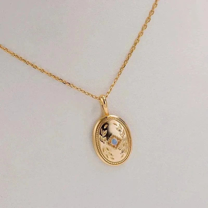 Gold necklace with an oval pendant on a light gray background