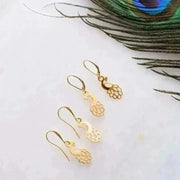 Gold peacock-shaped earrings on a white surface with a peacock feather.