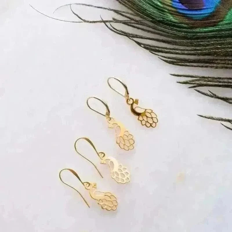 Gold peacock-shaped earrings on a white surface with a peacock feather.