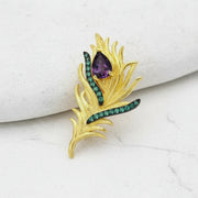 Gold brooch with purple and green gemstones on a white background