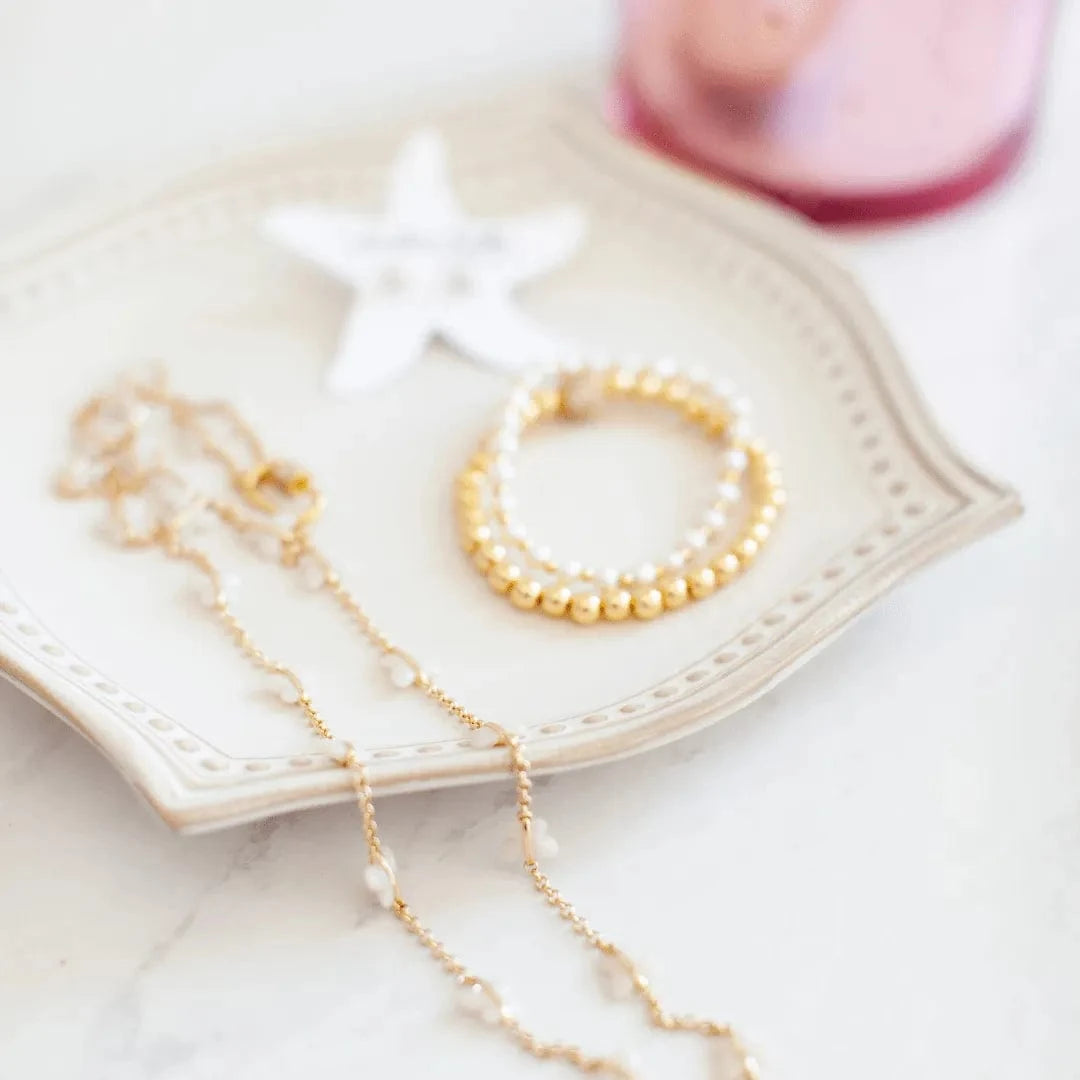 Pearl necklace and bracelet on a decorative plate with a pink heart in the background