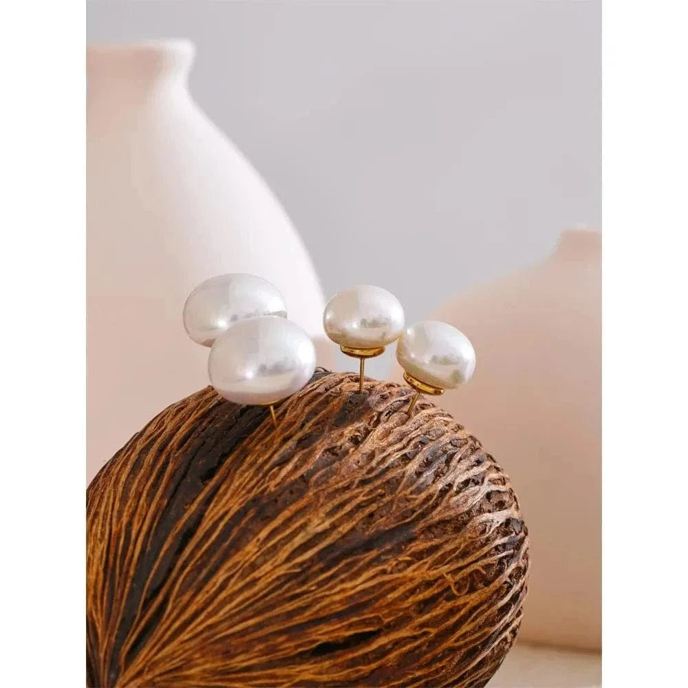 Pearl earrings on a textured brown surface with a white vase in the background