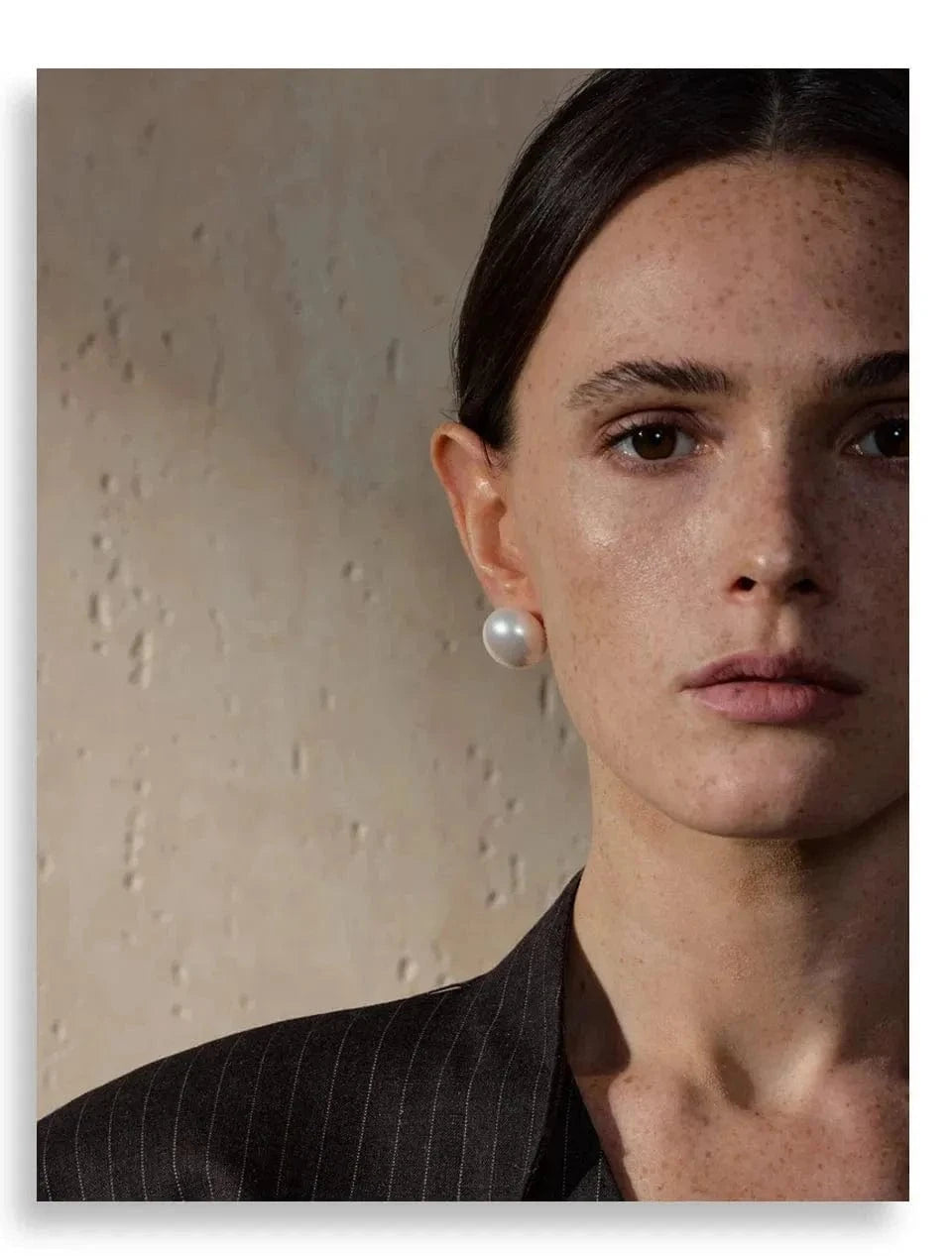 Close-up of a woman wearing pearl earrings against a neutral background