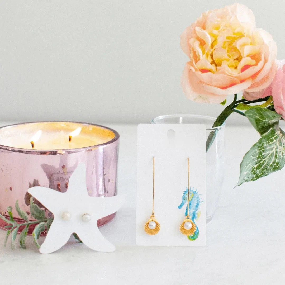 Pair of earrings on a card with a lit candle and flowers in the background