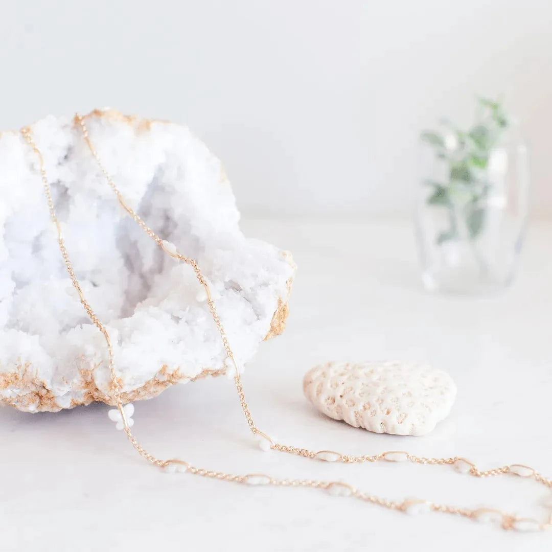 Gold necklace on a white surface with a marble rock and small plant in the background