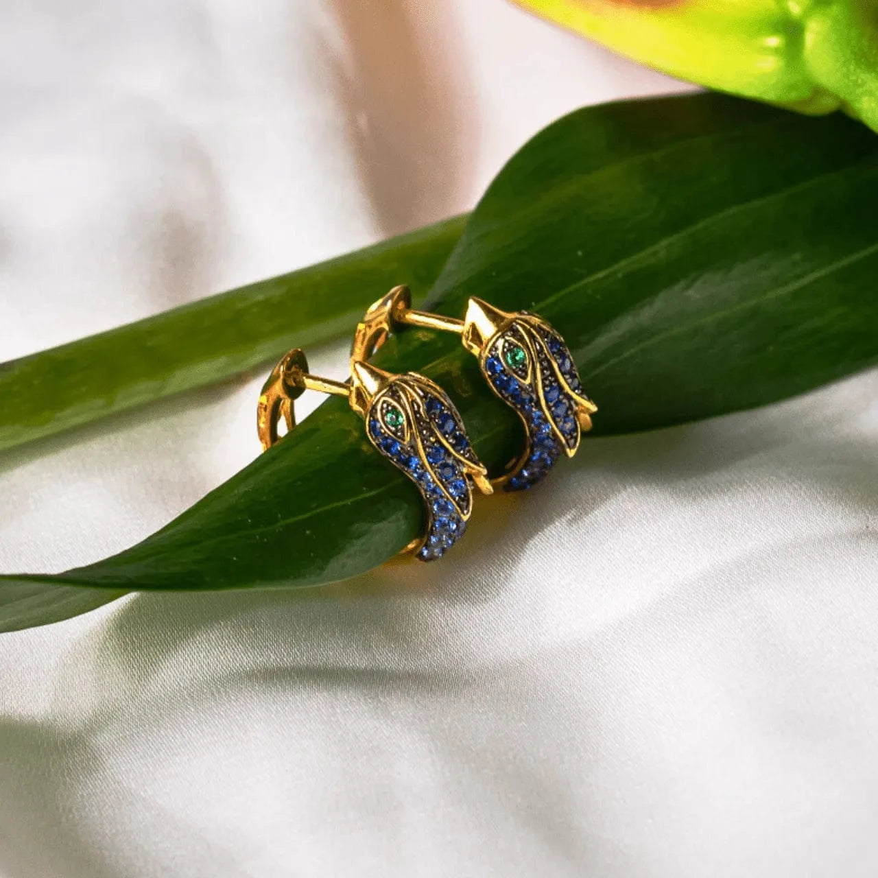 Gold hoop earrings with gemstones on a green leaf