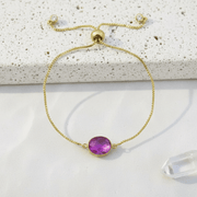 Gold bracelet with a purple gemstone on a textured surface
