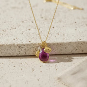 Gold necklace with a purple teardrop pendant on a textured surface