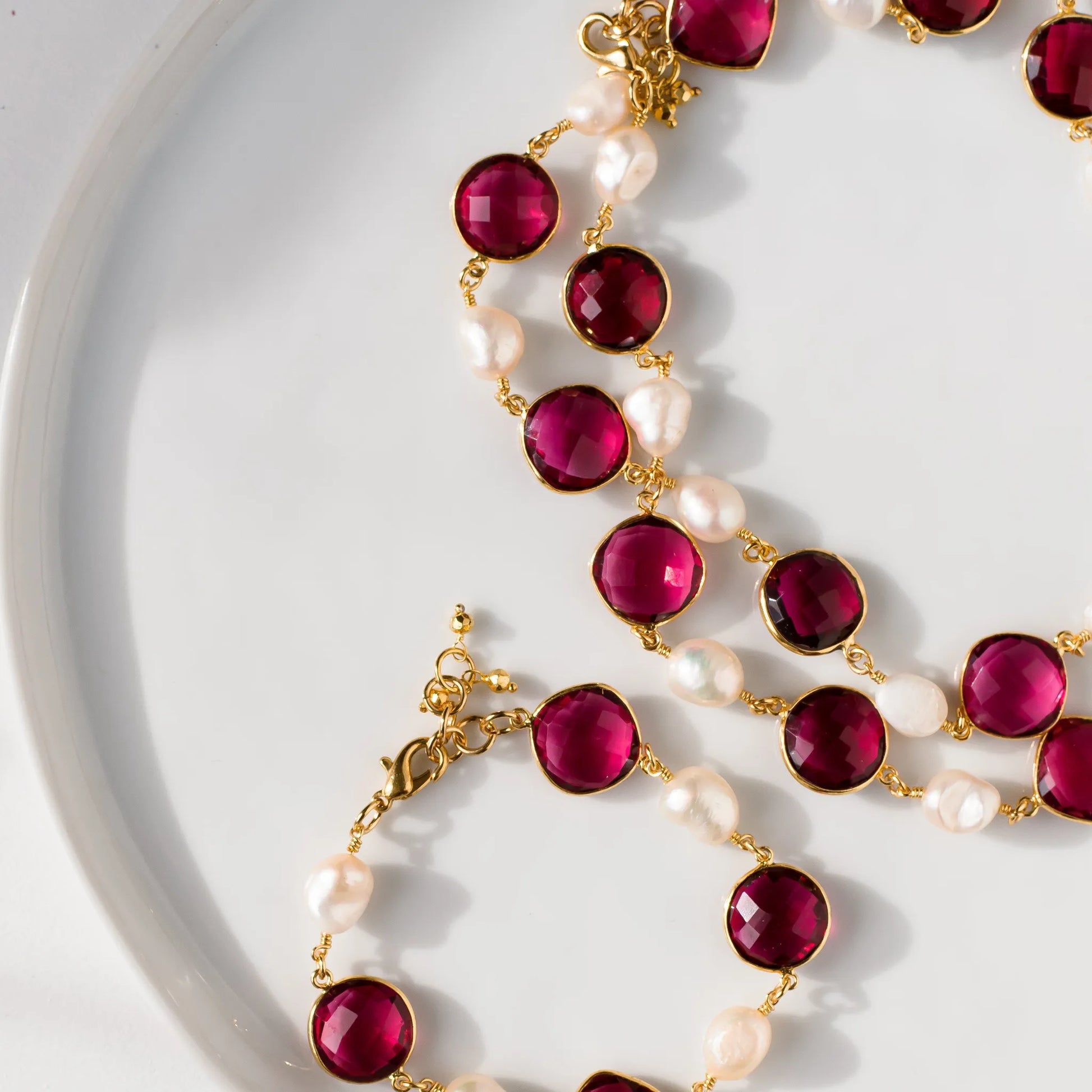 Necklace with red gemstones and pearls on a white plate