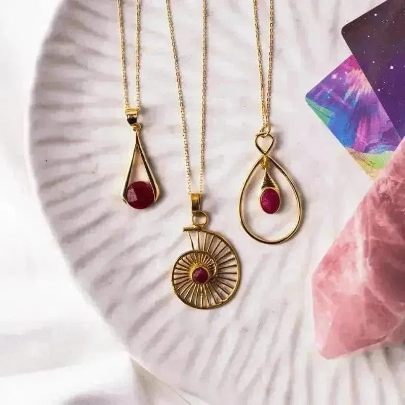 Three gold necklaces with red gemstones on a textured white surface.