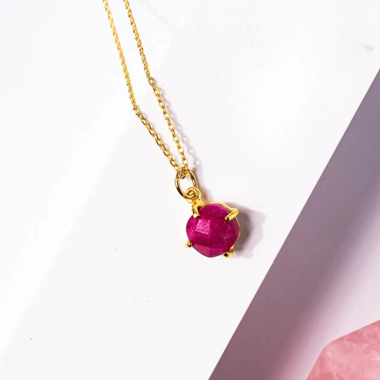 Gold necklace with a red gemstone on a white background