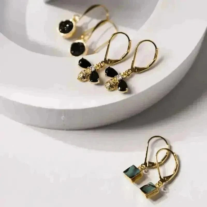 Gold earrings with black and green gemstones on a white surface
