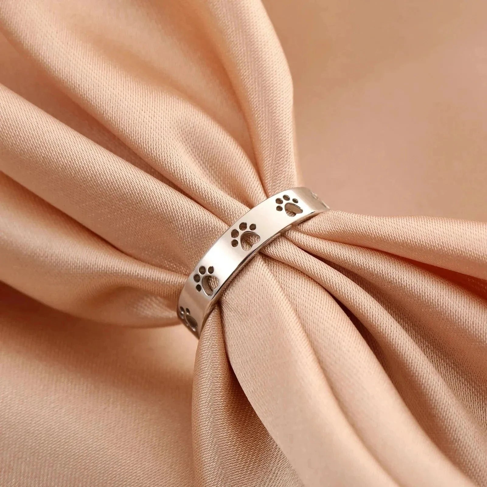 Silver ring with paw prints on a beige fabric background