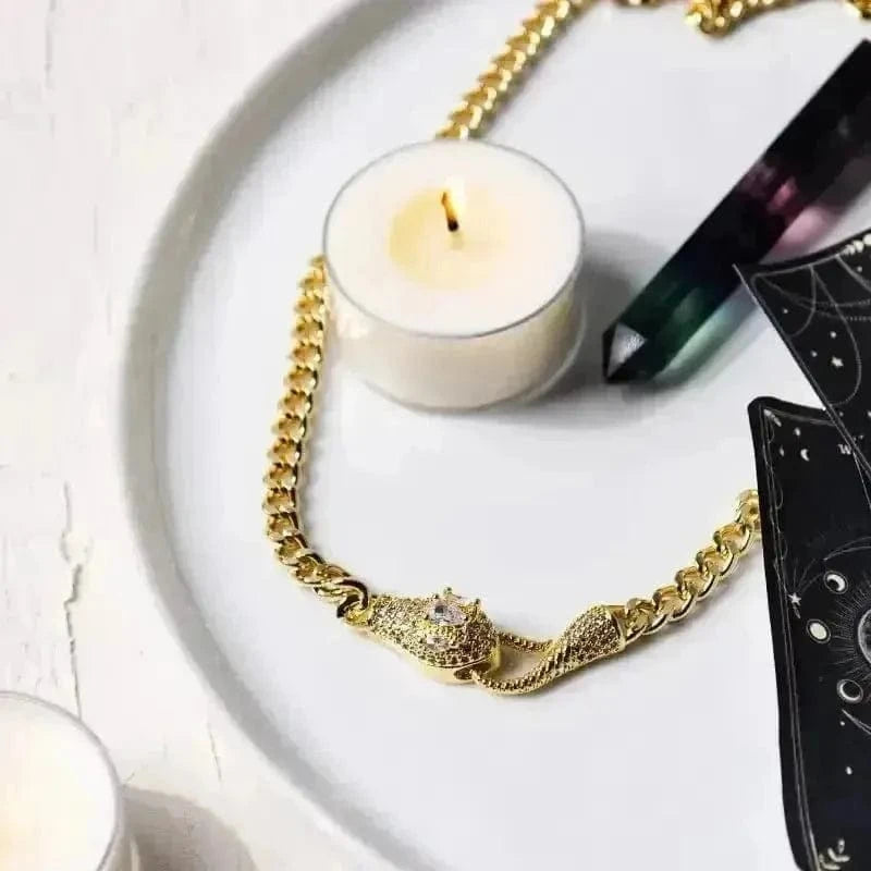 Gold chain necklace on a white plate with a lit candle and black book