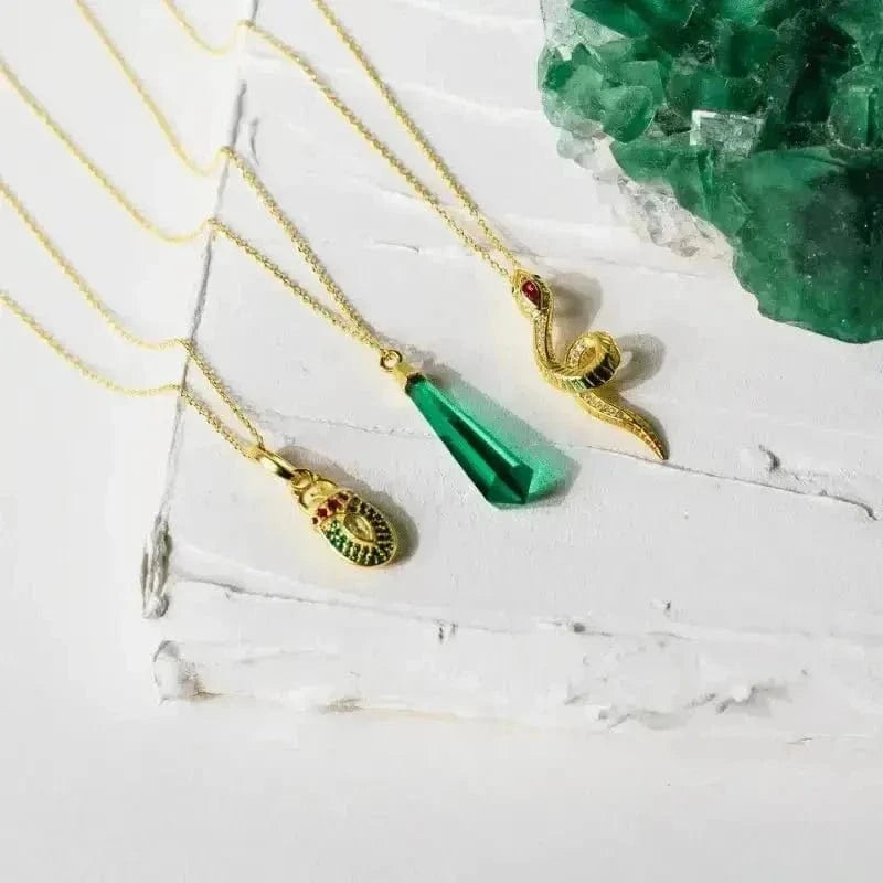 Gold necklaces with green pendants on a white surface with a green crystal in the background