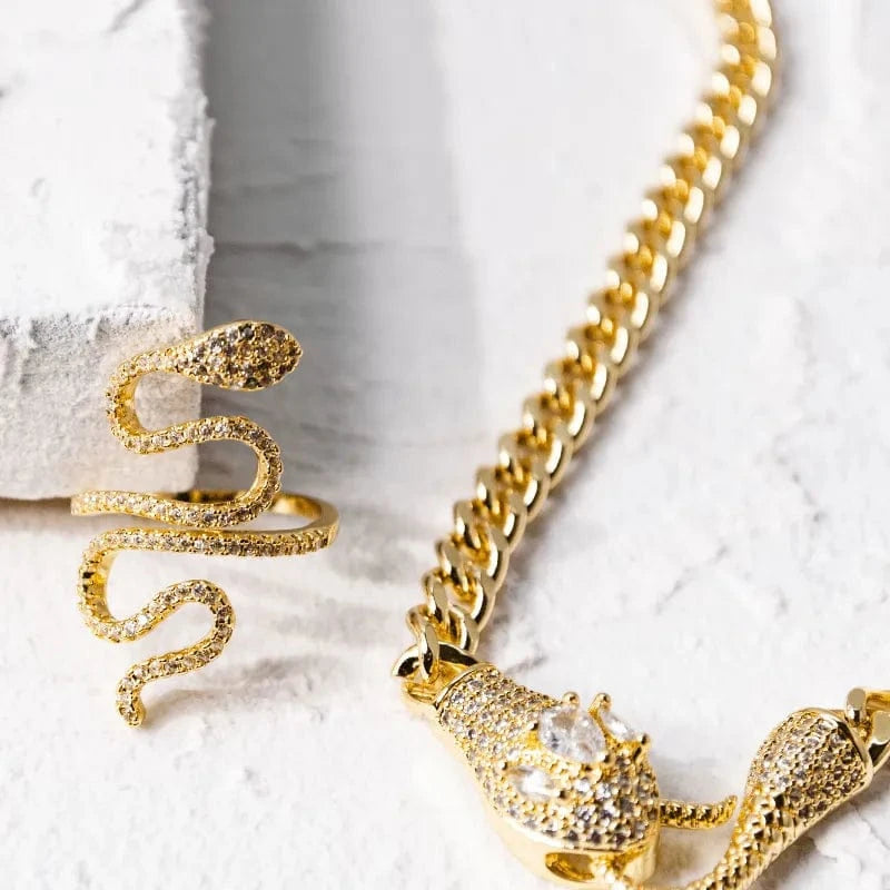 Gold snake-shaped ring and necklace on a textured white surface