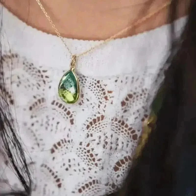 Green teardrop pendant necklace on a gold chain worn by a person with a white lace garment.